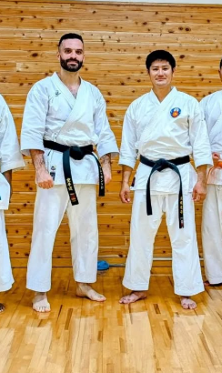 Alessandro in a black belt and white gi alongside another karate practitioner in a dojo.